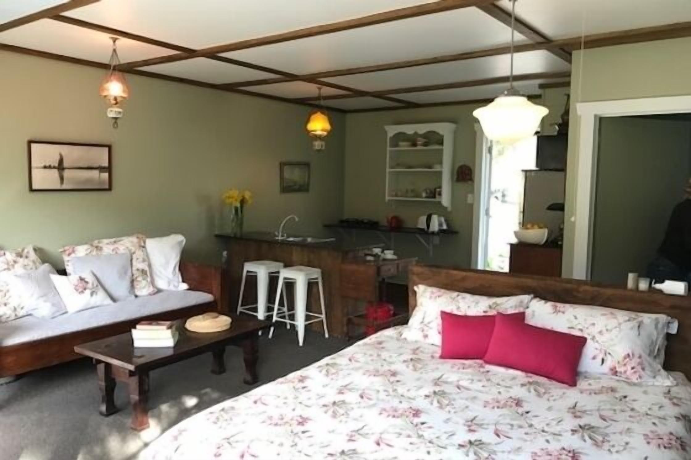 Een slaapkamer met een bed, een bank, een klein tafeltje en een keuken in de achtergrond.