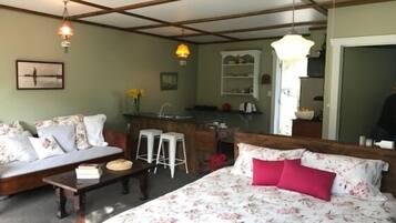 Een slaapkamer met een bed, een bank, een klein tafeltje en een keuken in de achtergrond.