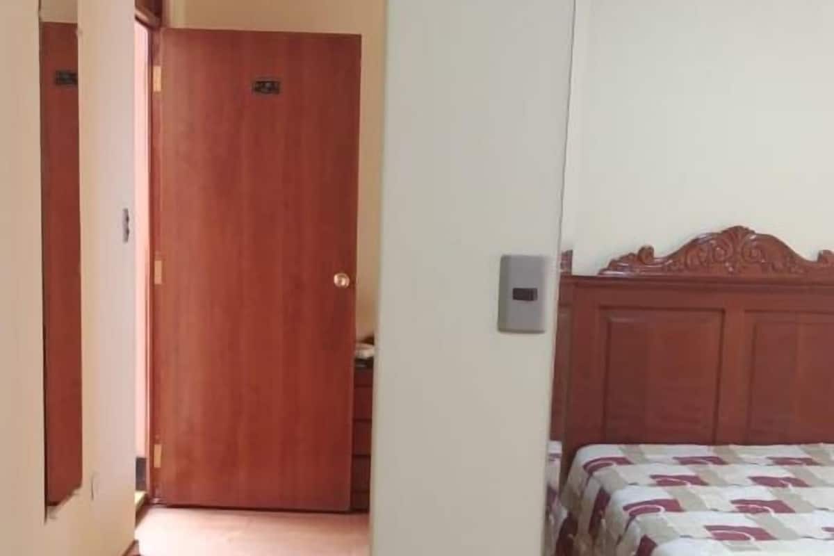 A bedroom with a wooden bed, a wooden door, and a hallway leading to another room.