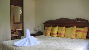 A neatly made bed with a white towel folded on it, a wooden headboard, and four yellow pillows with pink accents. - Hotel Dos Reynas (Characato)