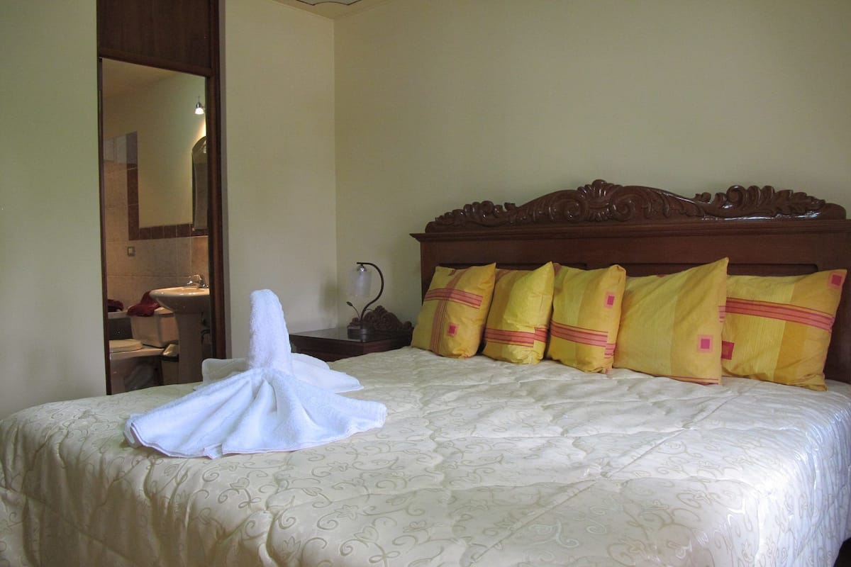 A neatly made bed with a white towel folded on it, a wooden headboard, and four yellow pillows with pink accents.