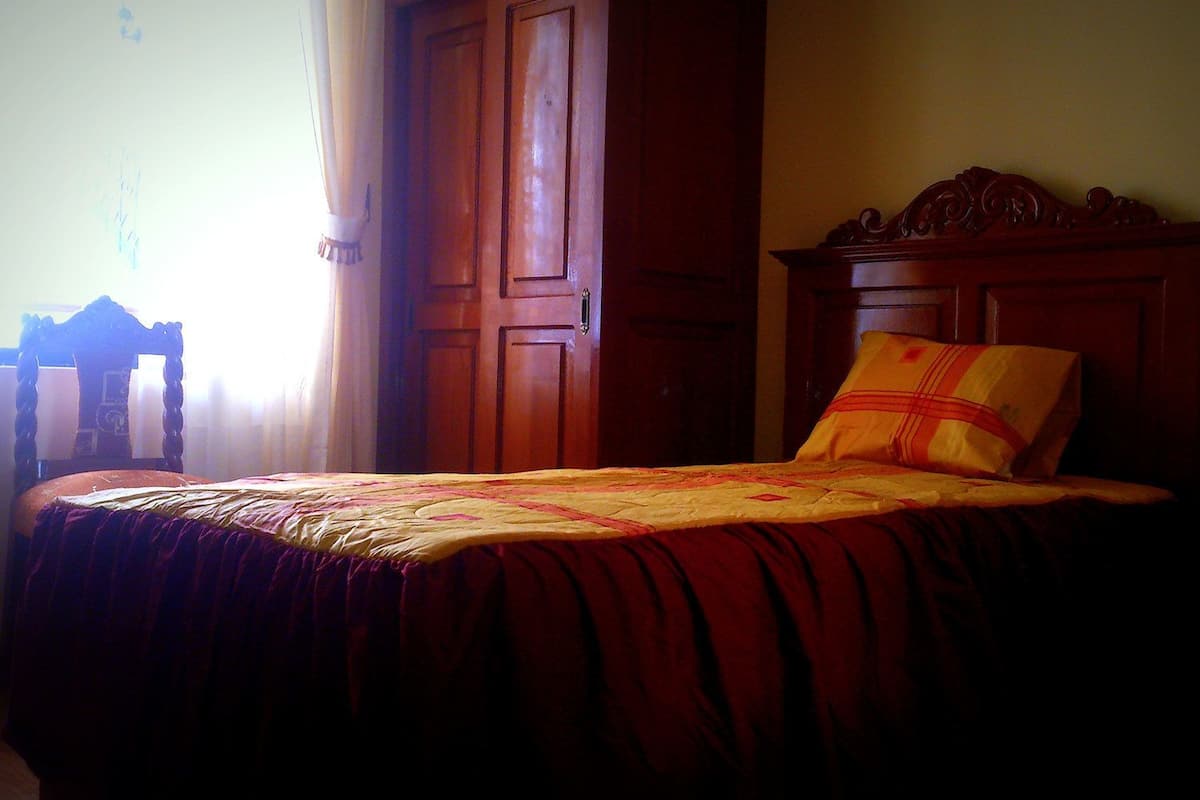 A bed with a wooden headboard, a red and yellow bedspread, and a single pillow.