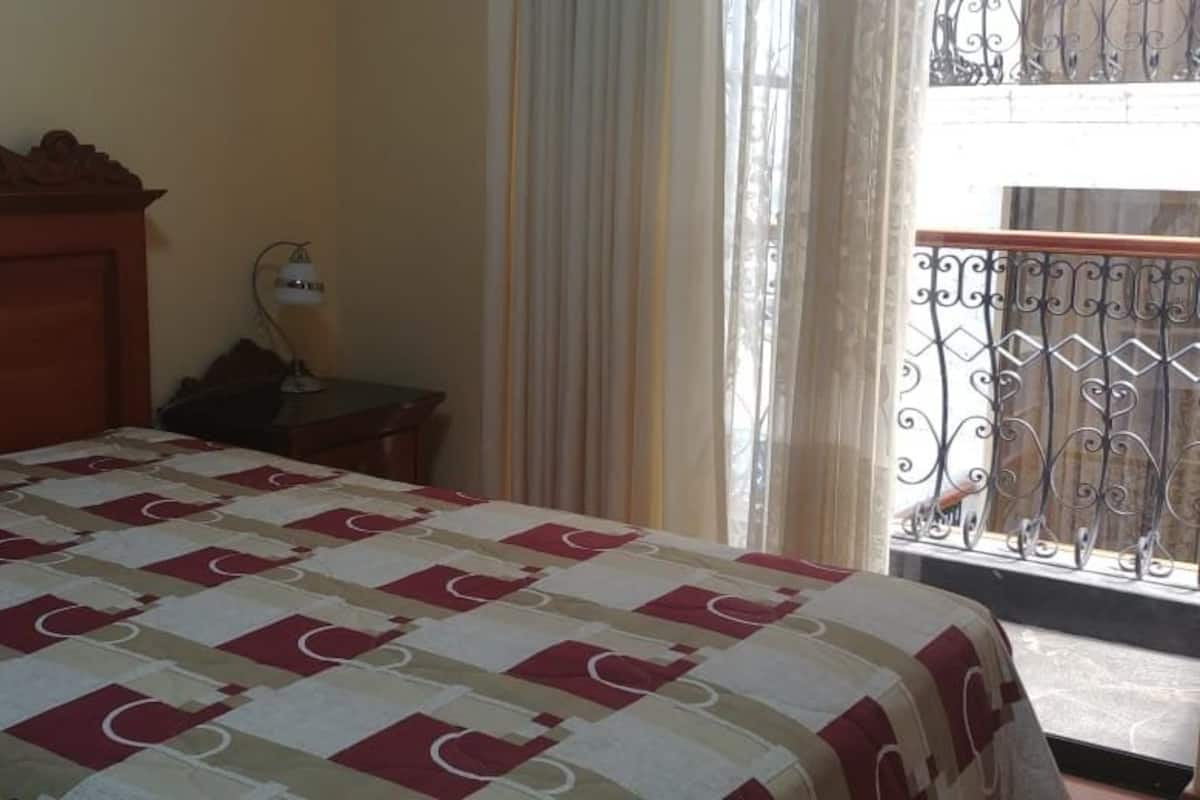 A hotel room with a bed, a nightstand, a lamp, and a balcony with a wrought iron railing.