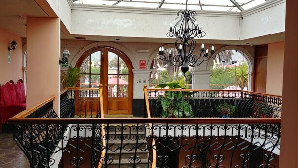 A spacious atrium with a high ceiling, a central staircase, and a view of the outside through large arched windows. - Hotel Dos Reynas (Characato)
