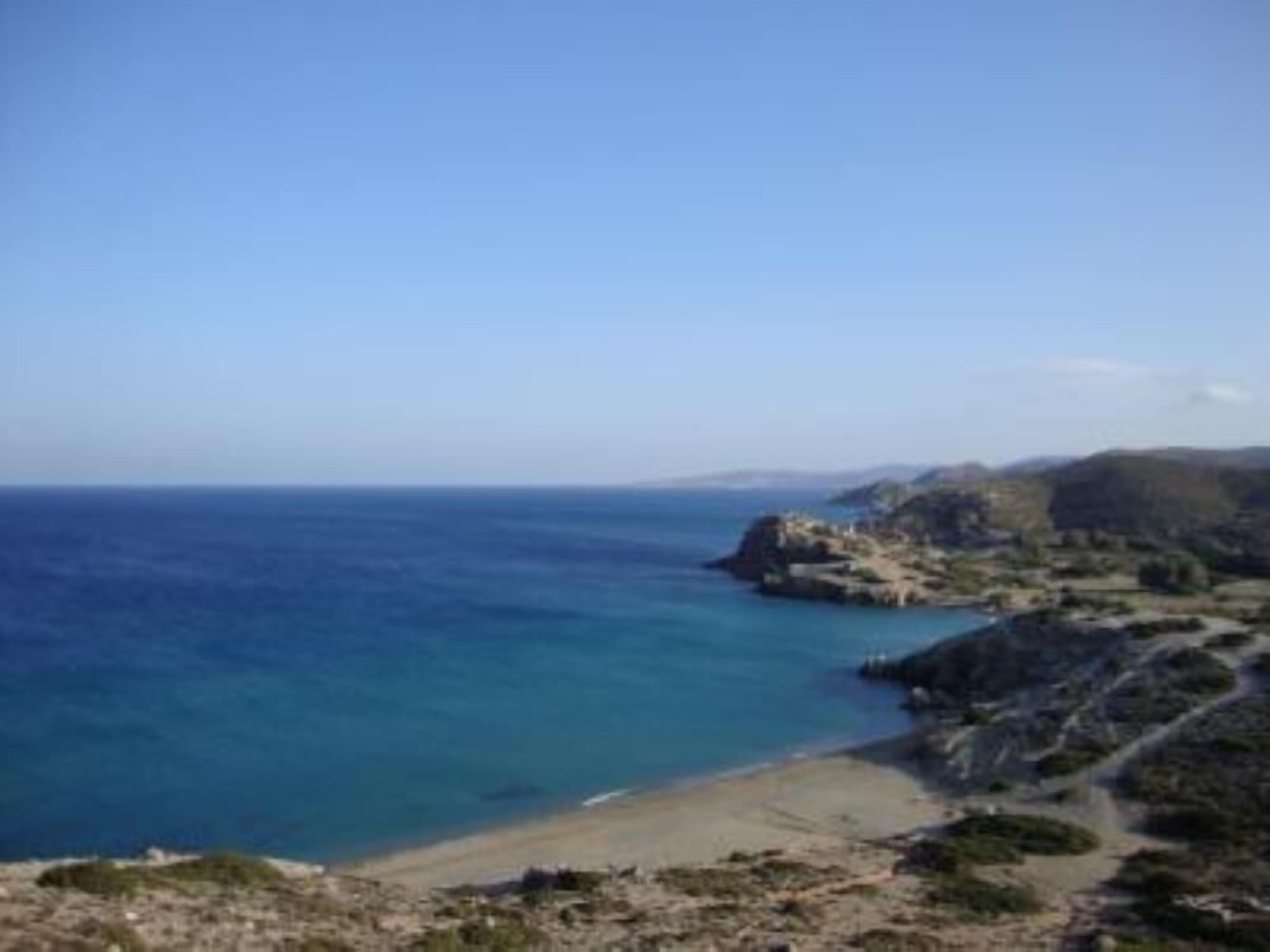A coastal landscape with a clear view of the sea, rocky terrain, and a path leading to a beach.