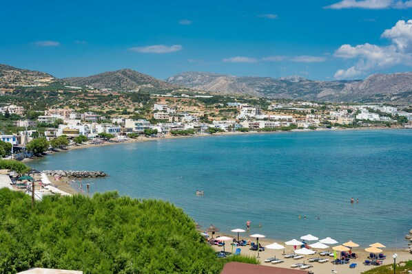 A coastal town with a beach, clear blue sea, and mountains in the background.