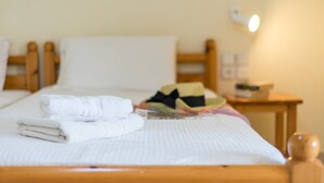 Ein ordentlich bezogenes Bett mit gefalteten Handtüchern, einem bunten Hut und einem Nachttisch mit Lampe.