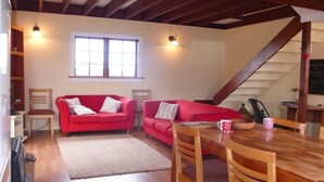 A cozy living room with a red sofa, wooden dining table, and a staircase leading to another level. - The Stablehand Quarters at Gunyah Country Estate by Mt Hutt (Methven (Mt Hutt))