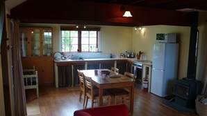 A compact kitchen with a dining area, wooden cabinets, a refrigerator, and a wood-burning stove. - The Stablehand Quarters at Gunyah Country Estate by Mt Hutt (Methven (Mt Hutt))