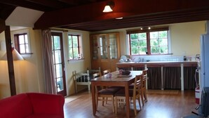 A dining area with a wooden table and chairs, a red sofa, and a kitchen in the background. - The Stablehand Quarters at Gunyah Country Estate by Mt Hutt (Methven (Mt Hutt))