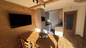 Ein Holzinterieur mit Esstisch, Stühlen, einem an der Wand montierten Fernseher und einer Küchenzeile mit Schränken und Spüle.