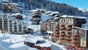 Ein schneebedecktes Resort mit mehrstöckigen Gebäuden, Skipisten und blauem Himmel.