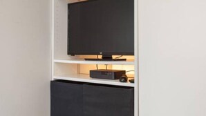 A television on a shelf with a remote control and a speaker below it. - Small Cozy studio with WiFi & cable (Southampton)