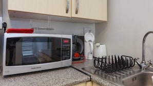 A kitchen with a microwave, coffee maker, and a dish rack. - Small Cozy studio with WiFi & cable (Southampton)