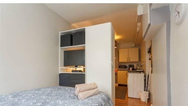 A bedroom with a bed, a built-in wardrobe, and a view into a kitchen area. - Small Cozy studio with WiFi & cable (Southampton)