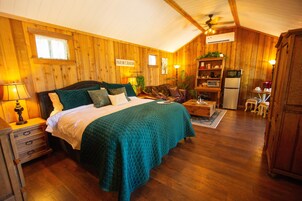Een gezellige kamer met een bed, een houten dressoir, een klein tafeltje en een kitchenette.