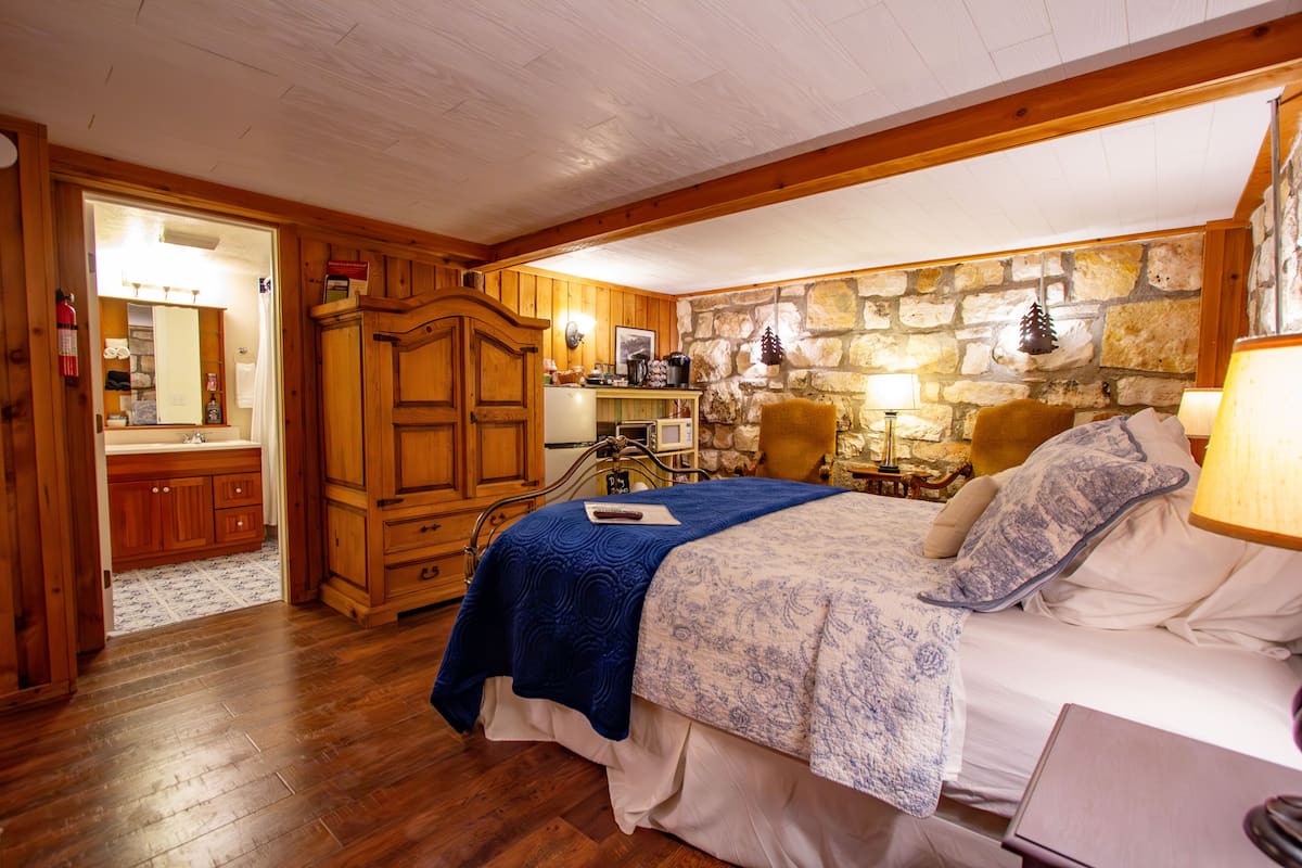 A bedroom with a wooden bed, a stone wall, and a wooden wardrobe.