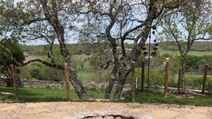 A stone fire pit surrounded by a gravel area with stone slabs, set in a natural landscape with trees and a stone wall in the background. - A Barn at the Quarry (Fredericksburg)