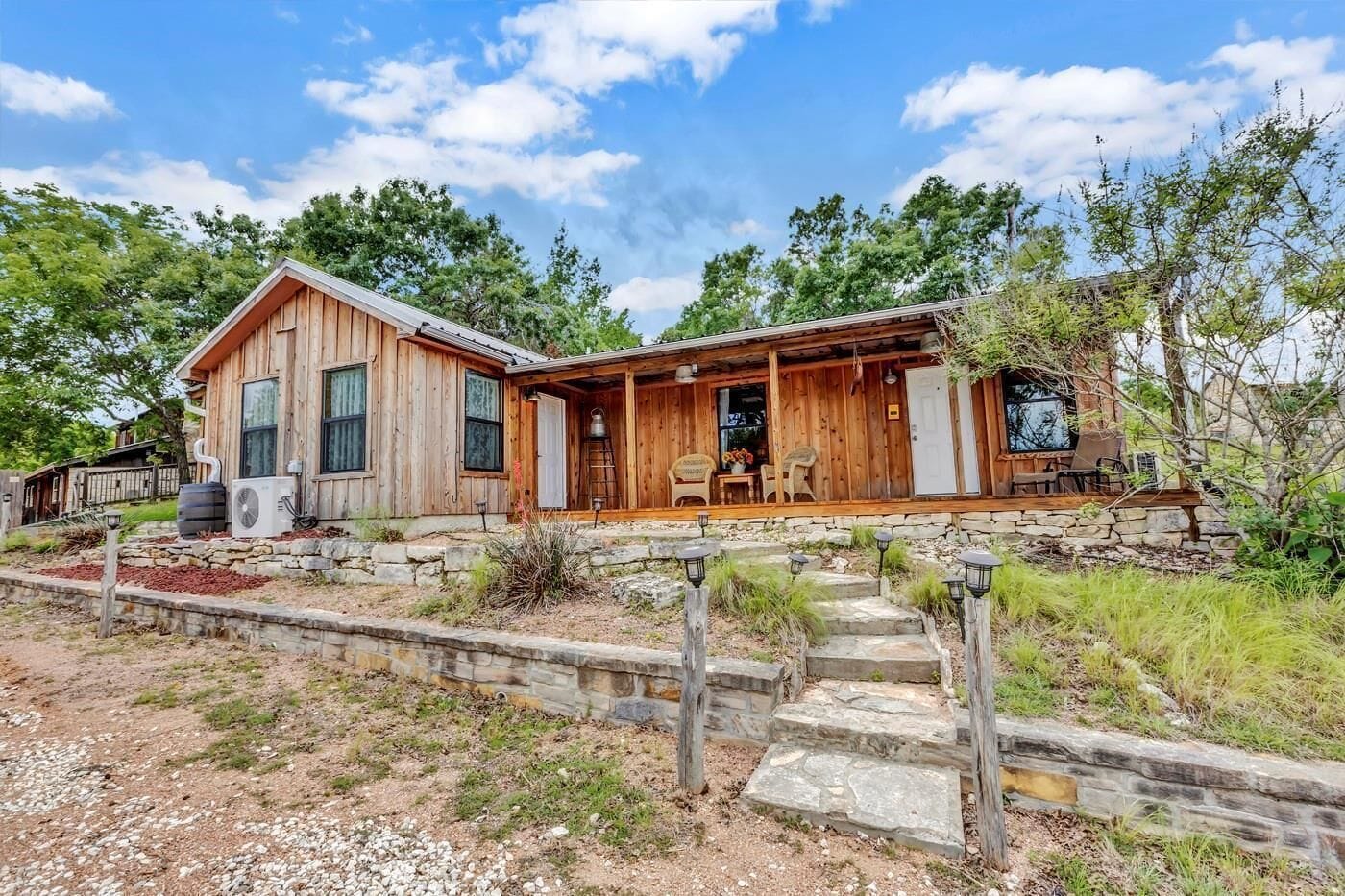 A wooden cabin with a stone foundation, a porch with outdoor seating, and a clear sky.