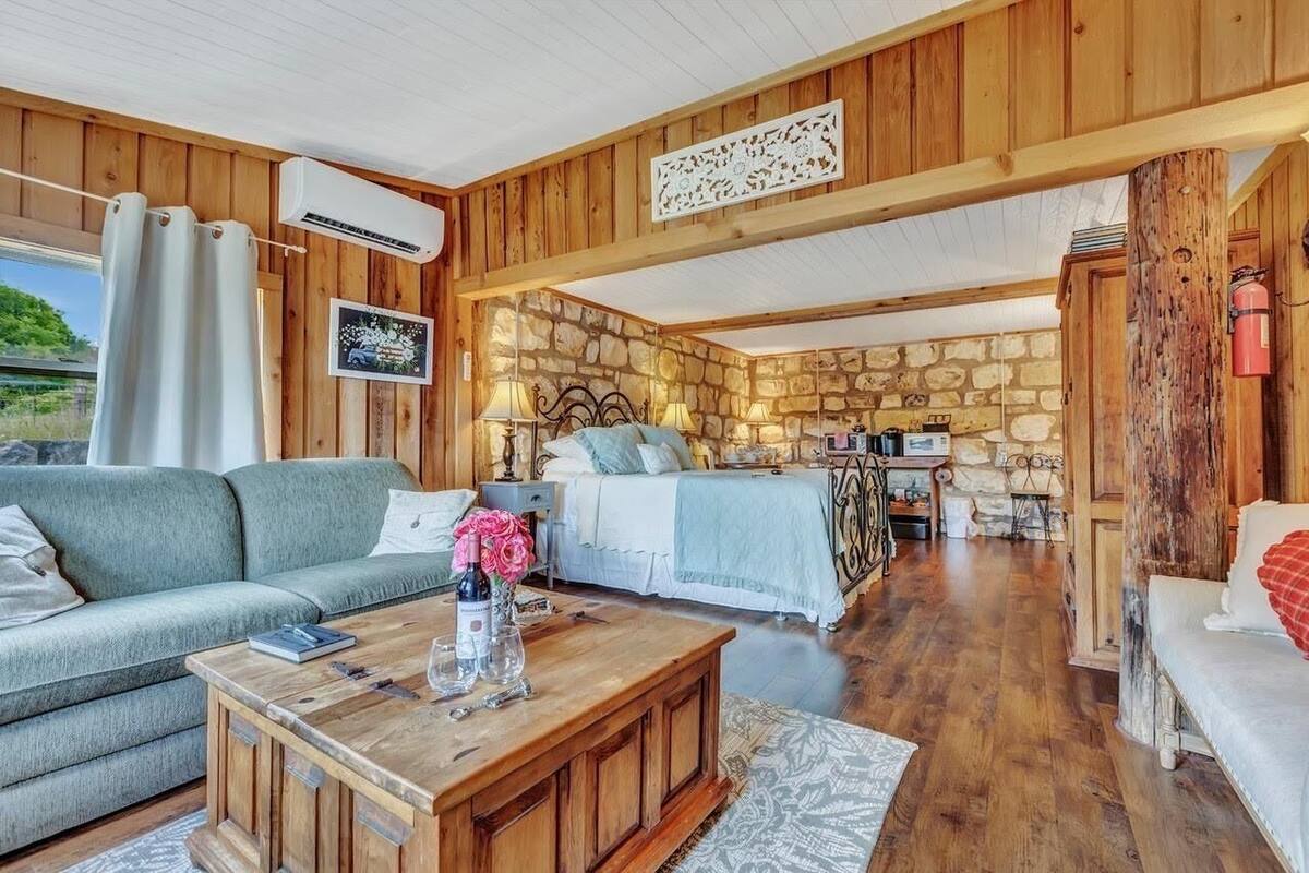 A cozy cabin interior with a stone wall, wooden ceiling, a sofa, a bed, and a dining area.