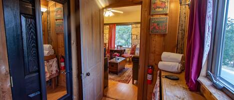 A wooden interior with a door leading to a room with a bed, a table, and a window with curtains.