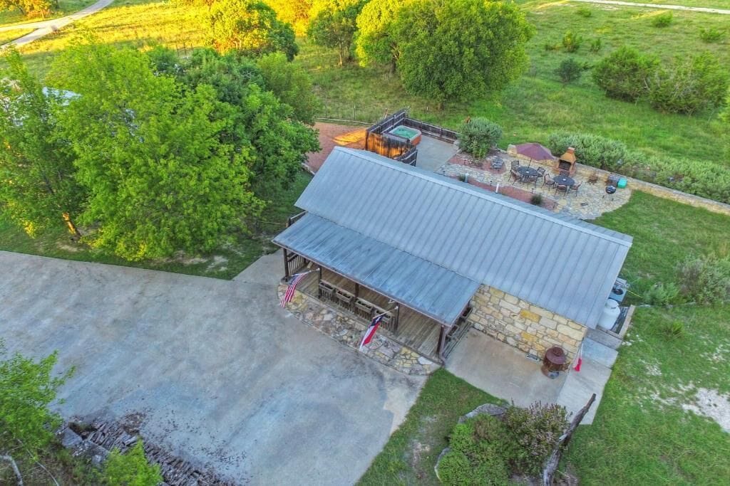 Vista aérea de una cabaña rústica con techo de metal, paredes de piedra y un patio con mobiliario exterior.
