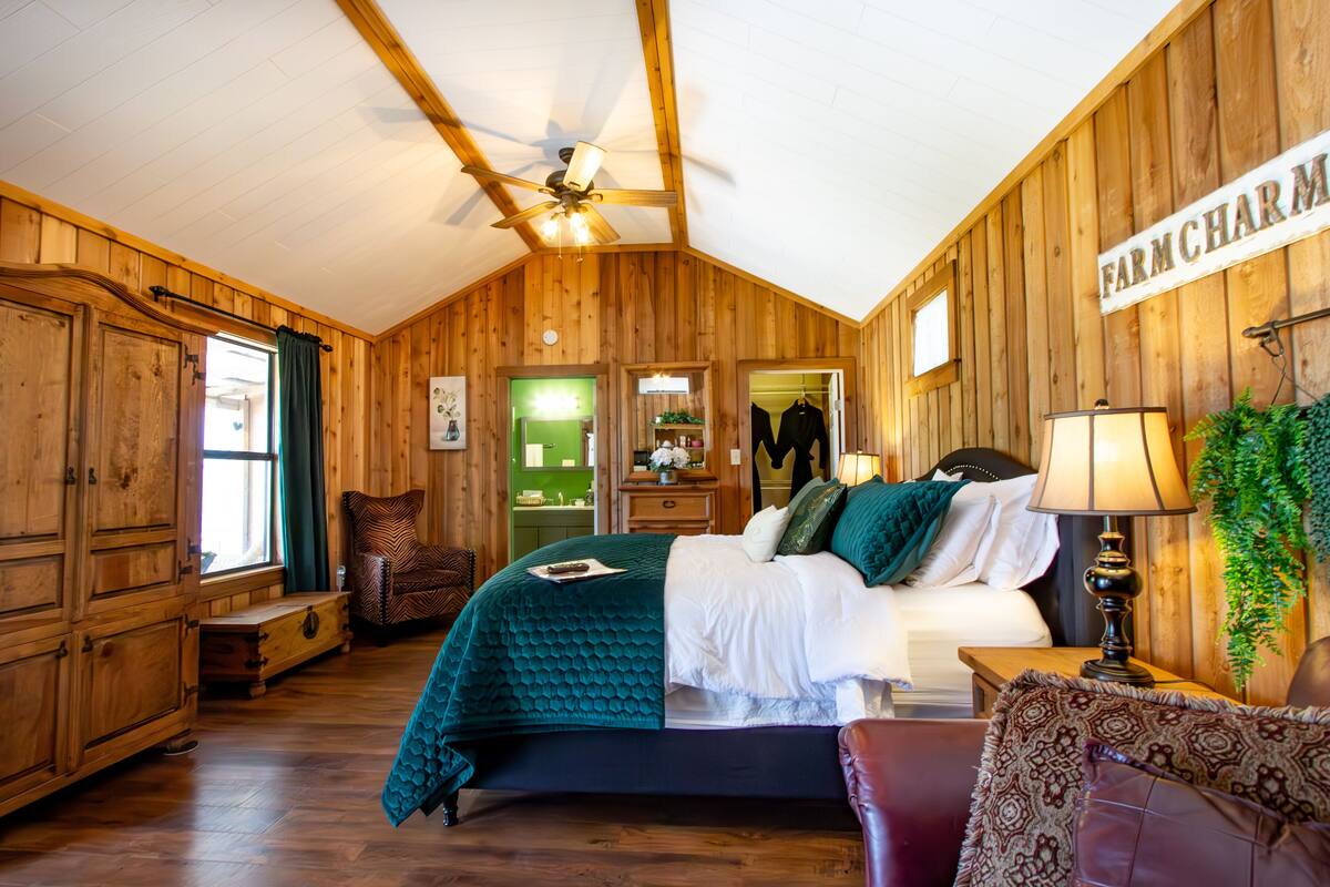 A rustic wooden room with a bed, a chair, a nightstand, and a window.