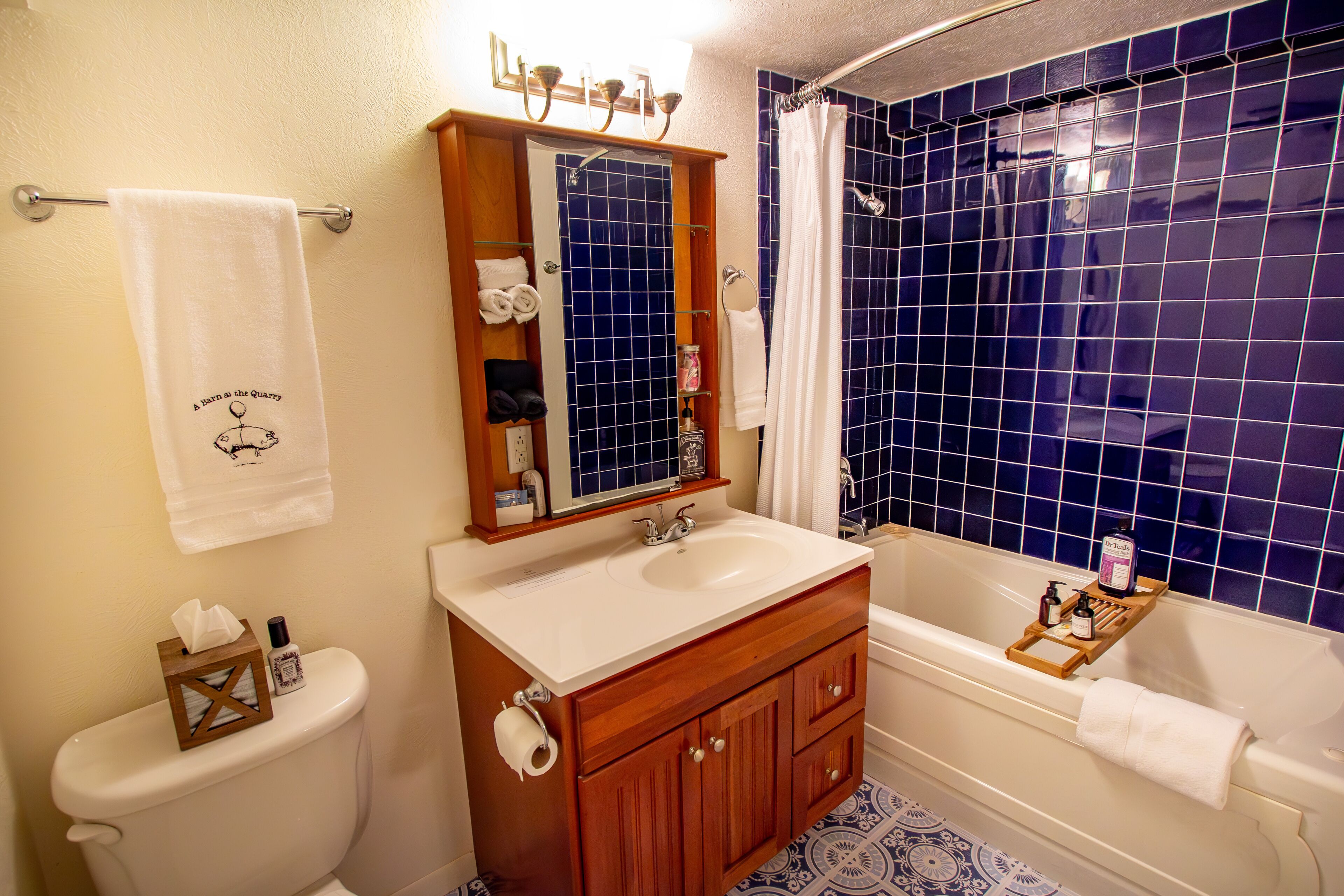 A bathroom with a white sink, wooden vanity, and a bathtub with a blue tiled shower wall.