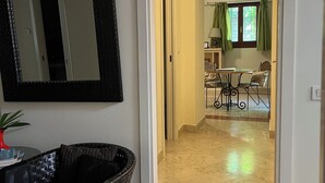 A room with a large mirror, a wicker chair, and a dining area with a table and chairs.