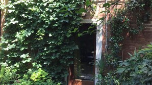 A brick building with a covered entrance, surrounded by lush greenery and a stone pathway.