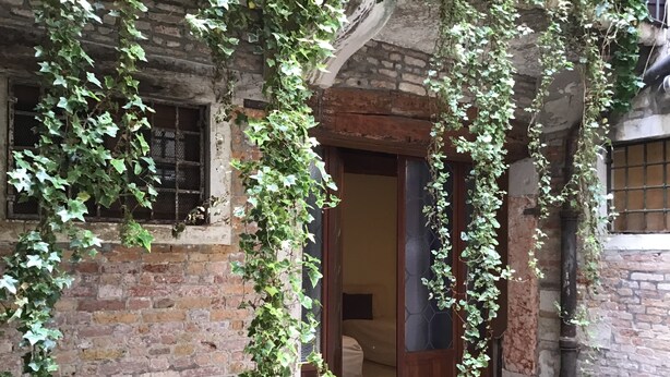 A rustic brick building with ivy-covered walls and a wooden door leading into a room.