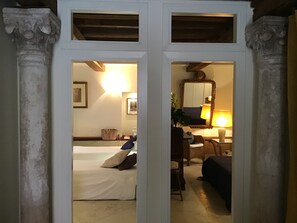 Ein Zimmer mit einem Bett, einem Schreibtisch und einem Stuhl. An der Wand hängt ein Spiegel und auf dem Schreibtisch steht eine Lampe.