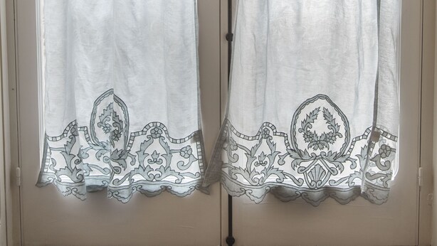 A double door with a frosted glass panel and a white curtain with a floral pattern and lace trim.