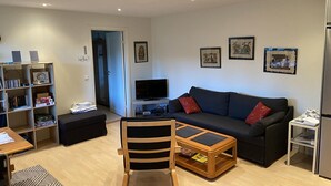 A living room with a sofa, TV, bookshelf, and a small table with a chair. - Guesthouse built on the owner's plot. close to beach, shop and golf course. (Trelleborg)