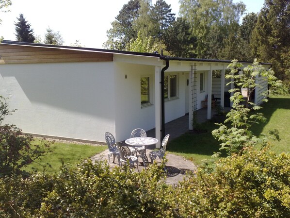Un edificio blanco con un patio cubierto, mobiliario exterior y un jardín.
