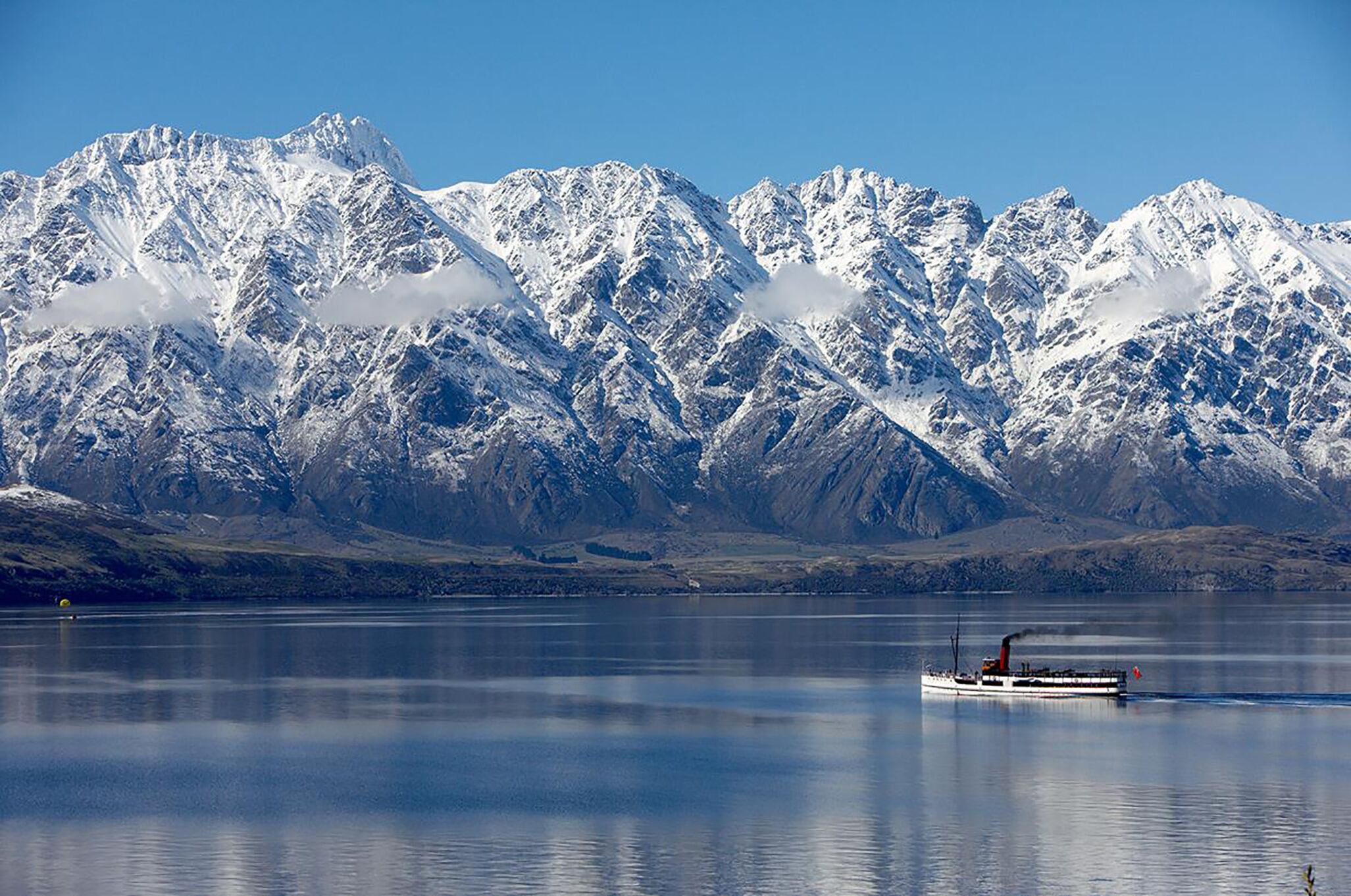A boat on a calm lake with snow-covered mountains in the background.