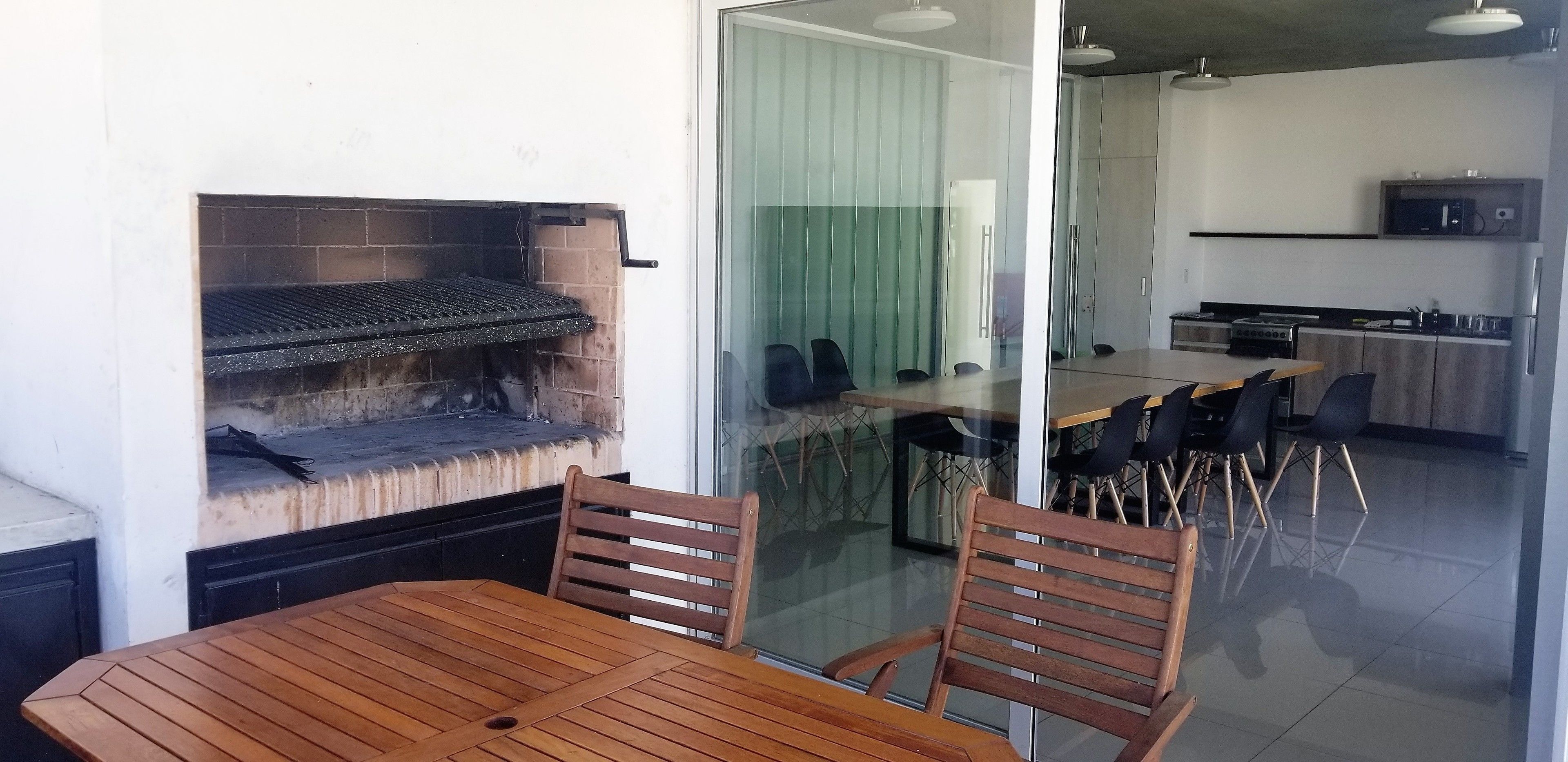 A modern kitchen with a built-in grill, a dining area with a table and chairs, and a glass partition separating the dining area from the kitchen.