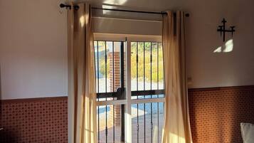Een kamer met een glazen deur naar buiten, een behang met patroon, een leren bank en een betegelde vloer.