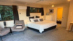A bedroom with a large bed, a desk, two chairs, a dresser, and a window with curtains.