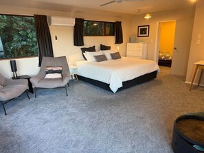 A bedroom with a large bed, a desk, two chairs, a dresser, and a window with curtains. - Seaclusion - Great for Multigenerational Families (Akaroa)