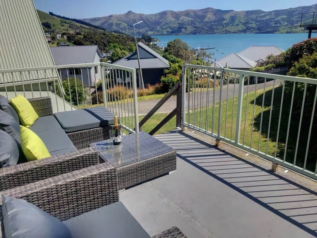 A balcony with outdoor furniture, a glass table, and a view of a lake and mountains.