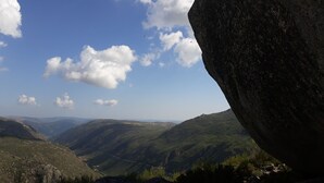 Un paysage montagneux avec un gros rocher au premier plan et un ciel dégagé.