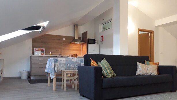 Un salon moderne avec un canapé foncé, une petite table en bois et une cuisine en arrière-plan.
