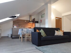 Una sala de estar moderna con un sofá oscuro, una pequeña mesa de madera y una cocina al fondo.