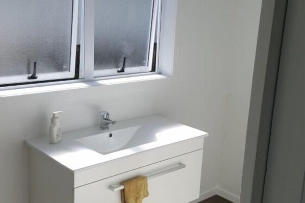 Un baño con un lavamanos blanco, una toalla colgada en la puerta y ventanas con vidrio esmerilado.