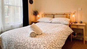 Una cama bien hecha con ropa de cama floral, una lámpara de noche y un reloj de pared.