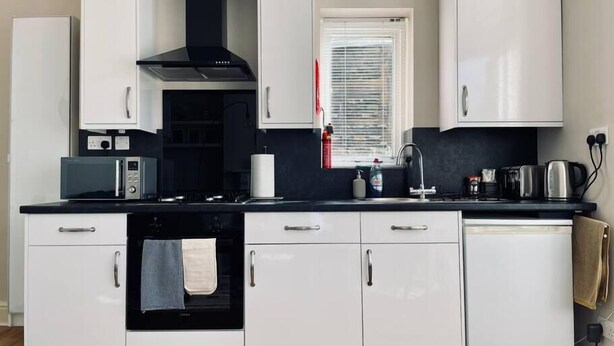 Een moderne keuken met witte kasten, een zwarte kookplaat, een magnetron, een spoelbak en een raam met jaloezieën.