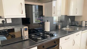 Una cocina moderna con armarios blancos, horno empotrado, estufa a gas, microondas y un lavamanos.
