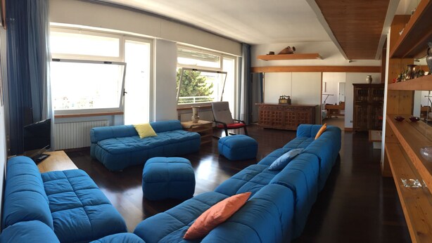A spacious living area with blue sofas, a wooden coffee table, and a kitchen area with wooden shelves. - Ruby Apartment 3 (Sanremo)