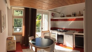 A compact kitchen with a dining area, a window with curtains, a radiator, and a clock on the wall. - Ruby Apartment 3 (Sanremo)